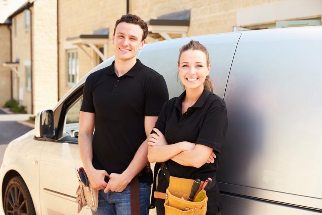 male and female tradespeople smiling in front of van
